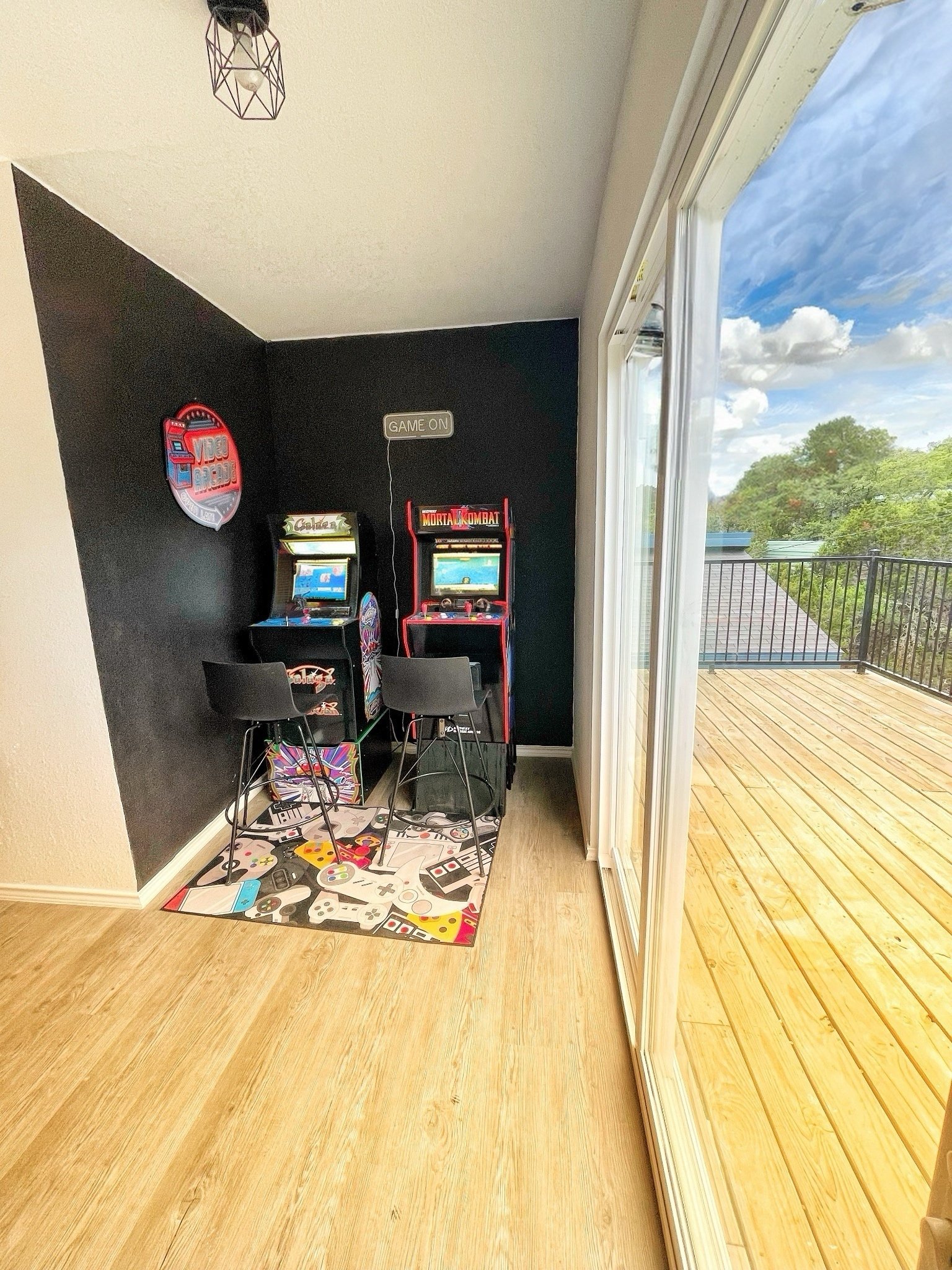 A cozy arcade corner with classic video game machines next to a sliding glass door leading to a wooden deck with scenic views of the outdoors.